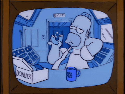 Simpsons gif. Homer is sitting at his desk at work and he's leaning back while chomping on a donut.