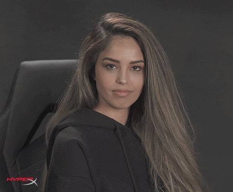Video gif. Youtuber Valkyrae looks at us with a seductive stare and tosses shimmery confetti up into the air in front of her face. 
