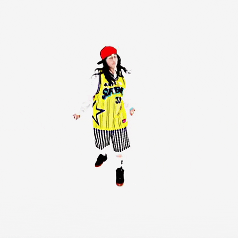 Music Video gif. From Billie Eilish's music video for "LUNCH", Billie is on a stark white background dressed in a white long sleeve shirt and a yellow and black jersey over the top, a red flat brim hat, and checkered long shorts with black sneakers on. She is standing and dancing by moving her hips and flapping her hands at her sides.