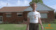 Movie gif. Standing in front of his home, Jon Heder as Napoleon Dynamite awkwardly waves and says "hi." 