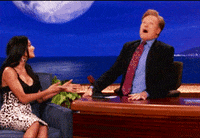 Celebrity gif. Conan O'Brien sitting at his desk, making frantic, wild circles with his head.