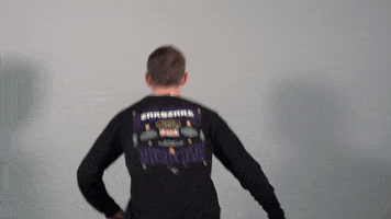 Video gif. Man jumps and turns towards us, landing with two thumbs up and a sarcastic expression on his face.