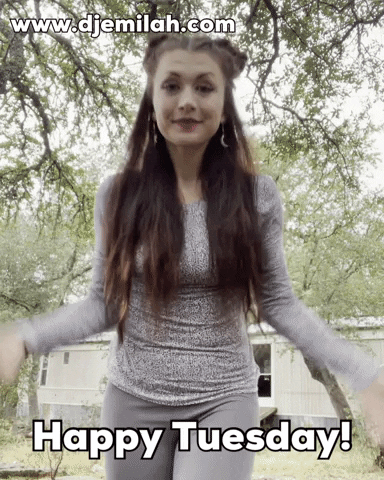 Video gif. Cheerful woman with long brown hair, magenta makeup, and dangling sun and moon earrings jumps in front of us and exclaims enthusiastically, "Happy Tuesday!," which appears as text.