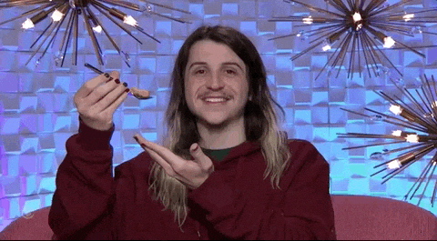 Reality TV gif. A contestant on Big Brother shows us something on a spoon during his interview and he smiles before slowly putting it in his mouth, savoring the flavor.