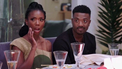 Reality TV gif. Brandy sits at a meal on My Kitchen Rules and raises a hand towards her mouth as she looks to the side in shock.