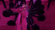Oscars 2024 GIF. Ryan Gosling is in the middle of his performance for I'm Just Ken and he puts the microphone back on the stand. The microphone stand is way too tall and Gosling shortens it, bringing it down to his height. 