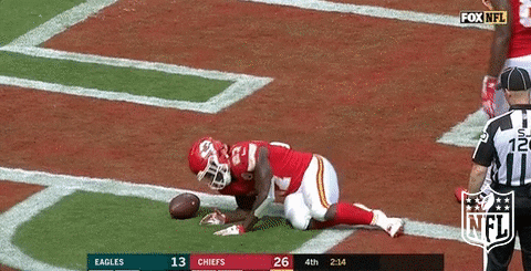 Sports gif. Kareem Hunt wears his helmet and uniform as he uses a football for a pillow and lies down with it in the middle of the field.