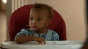 TV gif. Baby from Lethal Weapon. She stares up with her big eyes and plays with food that's on her tray.