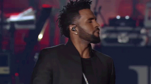 Celebrity gif. Jason Derulo is biting his lip on stage and smiling.