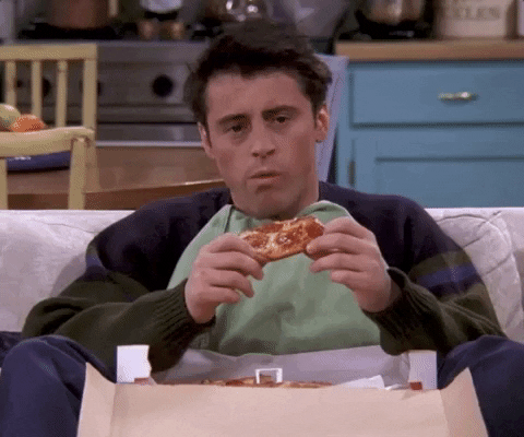 Friends gif. Matt LeBlanc as Joey sits on the couch with a box of pizza flung open between his legs. He holds a slice of pepperoni pizza and pauses in the middle of his bite to think hard about something. No thought can be found and he says with chewing, “I don’t know”