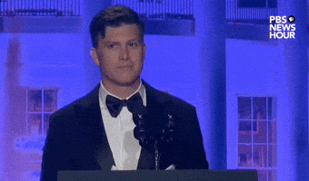 Video gif. Saturday Night Live's Colin Jost stands at a podium at the 2024 White House Correspondents' Dinner and surveys the crowd with a mischevious look in his eyes as he shuffles through his speech papers. He rapidly pulls out a sheet of paper, putting it at the back of the stack of paper in his hand.