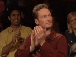 TV gif. Ryan Stiles on Whose Line is it Anyways sits in a chair in front of the audience. His eyes are wide as he claps and nods his head along with the audience. He then gives two big thumbs up.
