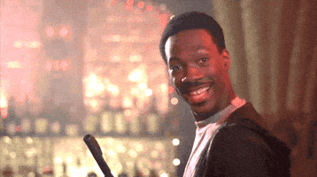 Movie gif. Eddie Murphy as Axel in Beverly Hills Cop looks over his shoulder and smiles with an open mouth as he holds up an enthusiastic OK with his hand. 
