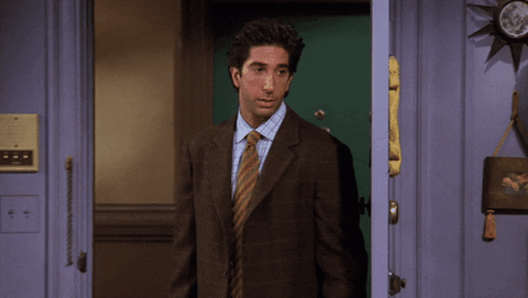 Friends gif. David Schwimmer as Ross stands near a door and looks annoyed as he gestures with his fists as if saying screw you. 