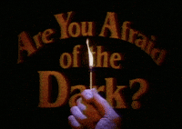 Text gif. Written in a haunting orange font, text reads "Are You Afraid of the Dark?" while a hand holds a singular burning match in front.