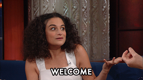 Celebrity gif. A smiling Jenny Slate reacts in wonder and excitement on The Late Show with Stephen Colbert, holding her hands up and bobbing in her seat. Text, “Welcome.”