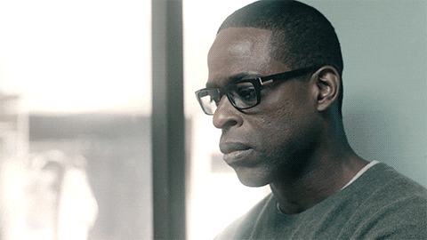 TV gif. Sterling K Brown as Randall in This Is Us. He leans against a wall and clenches his jaw in an attempt to hold back his tears. He takes his glasses off and pinches his nose bridge, before breaking into a cry.