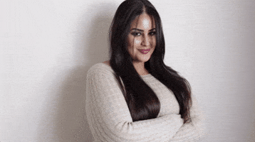 Video gif. A woman hugs herself and then giggles, leaning into herself shyly as she smiles. 