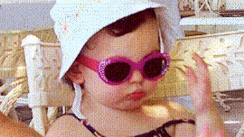 Video gif. A baby wears a hat and sunglasses and she moves to slide the glasses lower and raises her eyebrows, as if she can't believe what she's seeing. She pouts and throws a bit of shade before shoving the glasses back on.