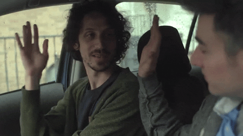 Video gif. Sitting in the driver’s seat of a car, a man offers the passenger a high five. The passenger reciprocates, giving the driver a high-five and a smile.
