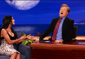 Celebrity gif. Conan O'Brien sitting at his desk, making frantic, wild circles with his head.