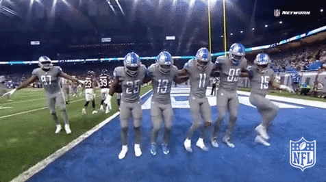Sports gif. Five Detroit Lions football players in uniform do a can-can line on the end zone.