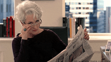 Movie gif. Meryl Streep as Miranda Priestly in The Devil Wears Prada sits at her desk with the newspaper in front of her. She looks up and whips her glasses off her face. She purses her lips as she thinks. 