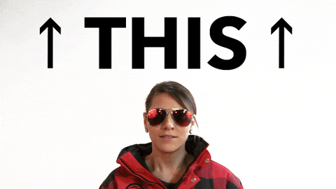 Video gif. A woman wearing aviator sunglasses and a winter coat points then looks up at text that reads, "This."