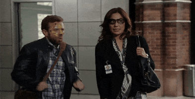 TV gif. Michaela Conlin as Angela Montenegro and TJ Thynes as Jack Hodgins on Bones both have face paint on their faces despite wearing work clothes. They both quickly turn away, cringes, as if trying to avoid someone.