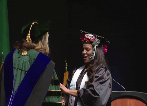 A woman is giving a thumbs-up after receiving her degree.