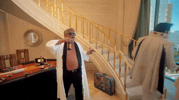 Video gif. An elderly man in a bathrobe wears sunglasses inside as he sips a beer and dances with a cigar in his hand. 