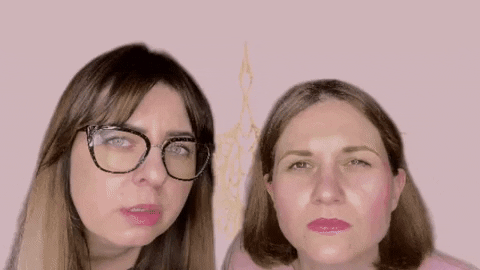 Video gif. Two women stand in front of a pink background that is a greenscreen. The woman on the left has long blonde hair and wears glasses and a long sleeve gray shirt. The woman on the right has short brown hair and a light pink long sleeve shirt. They squint judgementally at us with wide eyes and open mouths before backing up and dramatically shrugging. 