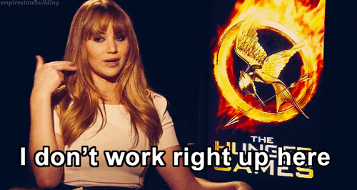 Celebrity gif. Actress Jennifer Lawrence sits in front of a Hunger Games poster, giving an interview. She points to her temple and says, "I don't work tight, up here."