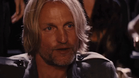 Movie gif. Woody Harrelson as Haymitch in The Hunger Games lifts a silver filigree flask and tilts his head in a cheers gesture.