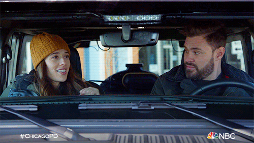 TV gif. Marina Squerciati as Kim in Chicago PD sits in the passenger seat and fist-bumps Patrick Flueger as Adam, who sits in the driver's seat.