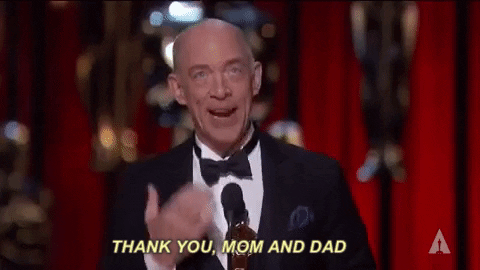 Celebrity gif. J.K. Simmons stands on the Oscars stage as he holds an award in his hand. With his other hand he slaps his heart and says with a big smile, “Thank you, Mom and Dad.”