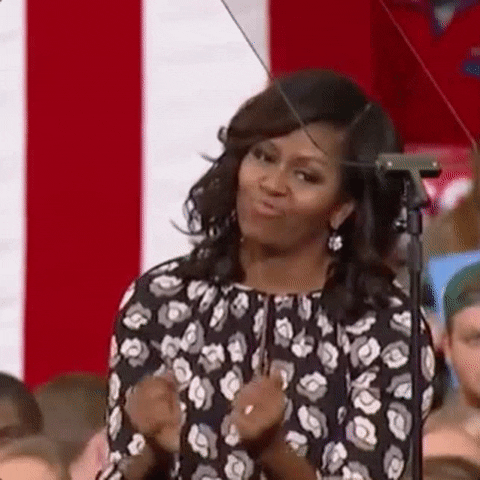 Celebrity gif. Michelle Obama does a little dance in her seat, moving her arms and shoulders. She tilts her head and purses her lips as she gets down.