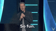 Video gif. On the 2024 Summer Game Fest stage presenter Geoff Keighley, wearing an open blue button-down shirt with a gray t-shirt underneath, into the microphone he is holding with his right hand, says,  'So fun.' The caption at the bottom of the gif reads the same.