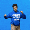 Digital art gif. Man wearing a blue sweatshirt that says "Climate action now" roundhouse punches the air, a comic strip-like "Pow!" symbol appearing in front of him, text inside of which reads, "Fight climate change!" everything against a blue background