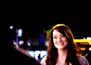 Celebrity gif. Emma Stone looks at someone with a smile, biting her lip, and holds up two big encouraging thumbs up.