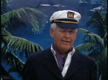 Video gif. Older man with white hair is wearing a suit and a sailor's cap. He looks at us for a second before shooting us a big thumbs up with a wink on the side.
