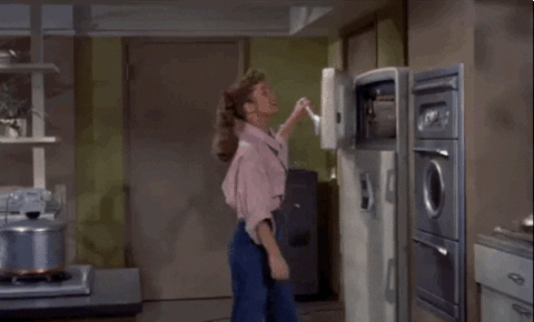 Movie gif. Debbie Reynolds as Susan in Susan Slept Here holds open the freezer door on the fridge and twirls herself around to rest her head in the freezer. She fans the door as an extra measure to cool herself off.