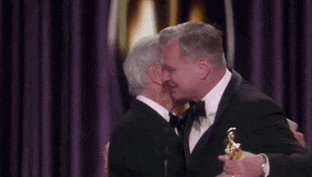 Oscars 2024 GIF. Steven Spielberg and Christopher Nolan share a two-armed hug and pat each other heartily on the back as Nolan wins Best Director. 