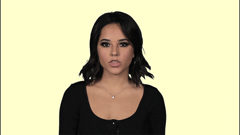 Celebrity gif. Becky G looks at us with a face full of attitude as she forms a big W with her fingers. She shakes her head as she says, “Whatever.”