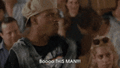 Movie gif. A scene from Half Baked. A man stands with a disgruntled looking crowd sitting behind him. He points angrily as if offended at someone, saying., “Boo this man! Boo!” He then grabs the hat off of his head and chucks it. The crowd behind him starts to get up and follow his protest.