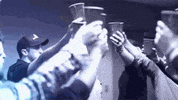 Video gif. Group of people have cups in the air and they toast one another before a Luke Bryan concert.