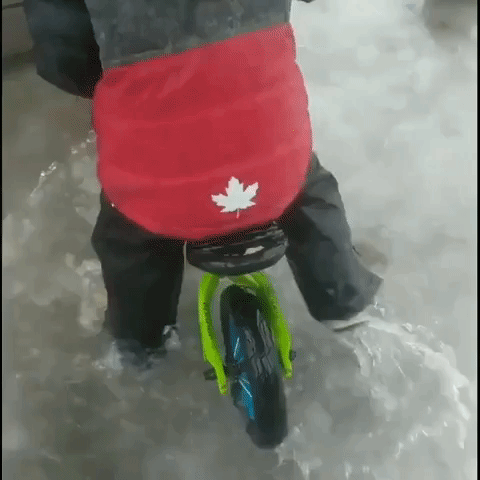 Young Boy Undeterred by Winter Storm Flooding Takes His Bike for a Wet Ride