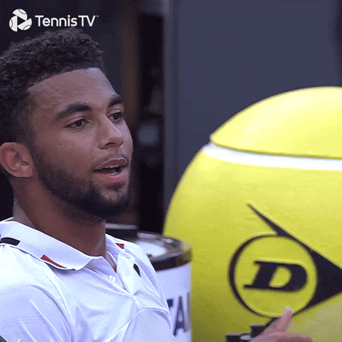 Sports gif. Arthur Fils sits on the sidelines of a tennis match, smiling and counting on his fingers, looking totally delighted.