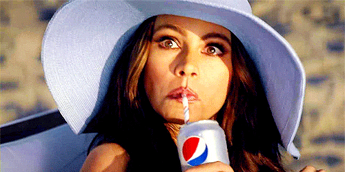 Ad gif. Sofia Vergara sits on a lounge chair on the beach. She looks up with wide eyes and sips on a can of Pepsi with a straw.