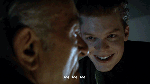 TV gif. A scene from Gotham with a sinister-looking young man laughing in the face of an uncomfortable older man in the foreground. Text, "Ha. Ha. Ha."